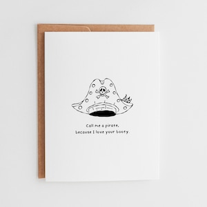 May include: A white greeting card with a brown envelope. The card features a black and white illustration of a pirate hat with a skull and crossbones. The text on the card reads, "Call me a pirate, because I love your booty."
