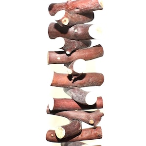 May include: A vertical hanging toy composed of multiple brown wooden branches stacked horizontally and secured with a thick tan rope. The ends of the branches are cut to reveal light-colored wood, creating a textured, layered appearance.