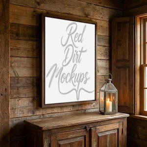 May include: A framed canvas with the text "Red Dirt Mockups" in a cursive font hangs on a rustic wooden wall. A candle lantern sits on a wooden cabinet below the canvas, next to a window with wooden shutters.