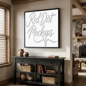 Puede incluir: Un lienzo cuadrado con marco negro con el texto "Red Dirt Mockups" en fuente cursiva. El lienzo está encima de una consola de madera negra con cajones, cestas y libros. Hay cerámica decorativa sobre la mesa.