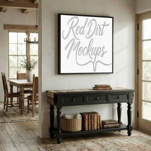 May include: A framed square print with the text "Red Dirt Mockups" in a cursive font hangs above a black console table. The table has three drawers, a lower shelf, and a woven basket. Books and a decorative runner are on the table.