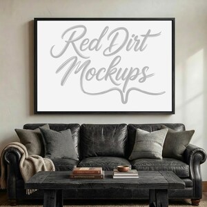 Könnte beinhalten: Ein gerahmtes weißes Bild mit dem Text "Red Dirt Mockups" in Schreibschrift hängt über einem schwarzen Ledersofa. Das Sofa ist mit grauen Kissen und einer beigen Decke geschmückt. Vor dem Sofa steht ein Couchtisch aus dunklem Holz.