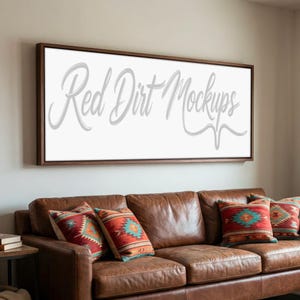 May include: A brown leather sofa with decorative pillows and a large framed canvas on the wall. The canvas displays the text "Red Dirt Mockups" in a cursive font. The pillows have a Southwestern design.