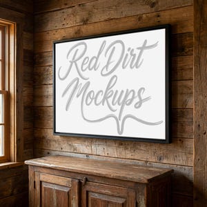 May include: A framed canvas mockup with the text "Red Dirt Mockups" in a cursive font. The black framed canvas is mounted on a rustic wooden wall above a wooden cabinet. The room has a warm, inviting feel.