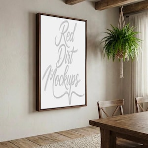Könnte beinhalten: Ein gerahmtes Bild mit dem Text "Red Dirt Mockups" in Schreibschrift. Der Rahmen ist dunkelbraun und die Leinwand ist weiß. Das Bild hängt an einer hellen Wand. Eine Hängepflanze und Holzmöbel sind ebenfalls zu sehen.