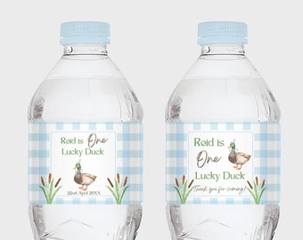 May include: Two clear plastic water bottles with blue and white checkered labels. The labels feature a cartoon duck with a blue hat and the text "Reid is One Lucky Duck". One label also includes the text "22nd April 20XX". The other label includes the text "Thank you for coming!"