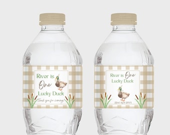 May include: Two clear plastic water bottles with brown and white checkered labels. The labels feature a cartoon duck, green reeds, and the text "River is One Lucky Duck". One label also includes the text "Thank you for coming!" and the other label includes the text "22nd April 20XX".