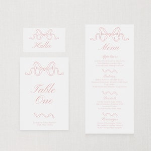 May include: A pink and white table card with a pink ribbon design. The card says "Table One" and "Felicity's Baby Shower 12th May 20XX".