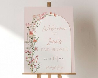 May include: A pink welcome sign with a floral archway design. The sign says "Welcome to Joni's Baby Shower" with the date "August 12, 20XX" and "24 days to go".