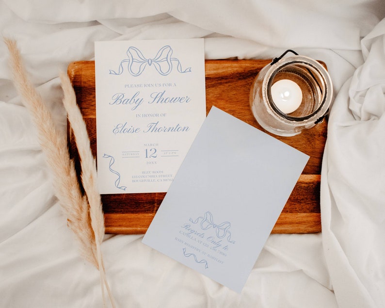 May include: A blue and white baby shower invitation with a blue ribbon design. The invitation reads "Please join us for a Baby Shower in honor of Eloise Thornton, March 12, 2024, 2:00 PM, 123 Main Street,  Someville, CA 95000". A separate card reads "Regrets Only to Carla at 123-456-7890".