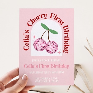 May include: Pink invitation with a red arch and the text "Celia's Cherry First Birthday". The arch has a cherry illustration with two pink cherries that look like disco balls. The text below the arch says "Join us to celebrate Celia's First Birthday" and includes the date, time, and address.