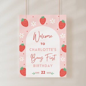 May include: A pink welcome sign with a strawberry theme. The sign says "Welcome to Charlotte's Berry First Birthday June 22 20XX".