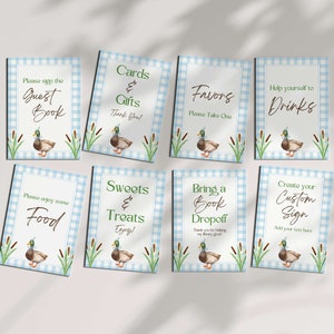 May include: Eight blue and white gingham signs with a duck illustration and text. The signs say "Please sign the Guest Book", "Cards & Gifts Thank You", "Favors Please Take One", "Help yourself to Drinks", "Please enjoy some Food", "Sweets & Treats Enjoy", "Bring a Book Dropoff Thank you for helping my library grow", and "Create your Custom Sign Add your text here".