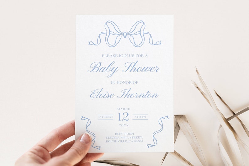 May include: A light blue baby shower invitation with a blue ribbon bow at the top. The invitation reads "Please join us for a Baby Shower in honor of Eloise Thornton. Saturday, March 12 at 2 PM. Blue Room, 123 Columbia Street, Boughville, CA 08765."