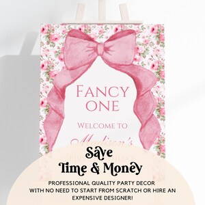 Op de afbeelding: Een roze en wit bedrukbaar bord met een grote roze strik en een bloemenpatroon. Het bord zegt "Fancy One" en "Welkom bij Madisons eerste verjaardag. Bespaar tijd en geld. Professionele partydecoratie van hoge kwaliteit, zonder dat je van scratch moet beginnen of een dure ontwerper hoeft in te huren!"
