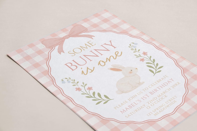 Op de afbeelding: Een roze en witte geruite uitnodiging met de tekst "Some Bunny is One". De uitnodiging bevat een aquarel illustratie van een konijn en bloemaccenten. De uitnodiging is voor Mabel's 1e verjaardag.