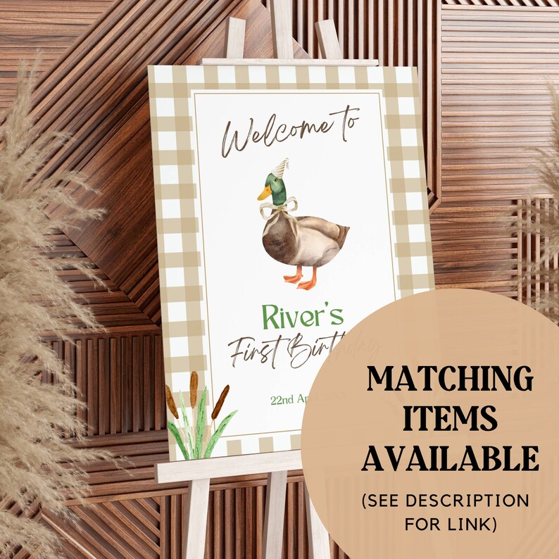 May include: Welcome to River's First Birthday party sign with a brown and green duck wearing a party hat and a bow. The sign has a brown and white gingham background with green reeds.