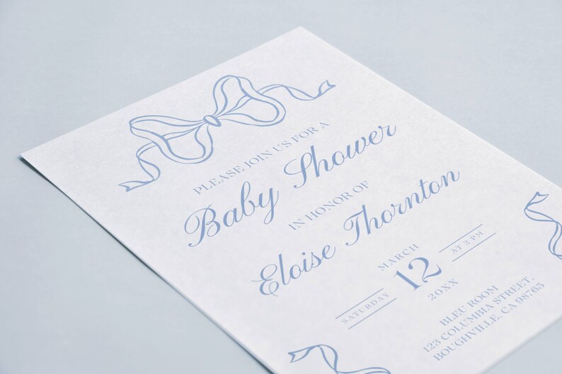 May include: A blue and white baby shower invitation with a blue ribbon bow at the top. The invitation reads "Please join us for a Baby Shower in honor of Eloise Thornton. Saturday, March 12, 20XX at 2 PM. Bleu Room, 123 Columbia Street, Boughville, CA 98765."