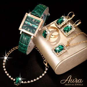 Puede incluir: Un conjunto de joyas y un reloj verde esmeralda. El reloj tiene una esfera cuadrada con números romanos y una correa de cuero verde. El conjunto incluye pendientes, un anillo, un collar y una pulsera, todos con piedras de color esmeralda.