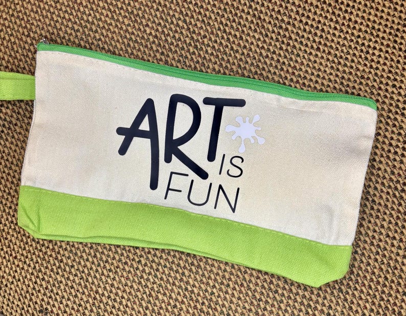May include: A rectangular canvas pencil case featuring a cream-colored body with a bright green bottom panel and matching green zipper. The front displays the black text ART IS FUN with a small white paint splatter graphic above the word ART.