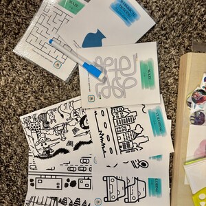 May include: A set of educational activity cards featuring mazes, tracing exercises, and coloring pages with black line art illustrations. The cards include text such as MAZE, WHIMSICAL TRACING, and COLORING, accompanied by a blue and white dry-erase marker.