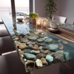Pu&ograve; includere: Un tavolo da pranzo rettangolare con una superficie trasparente e lucida, che mostra un design di ciottoli di fiume incastonati in resina blu. Il tavolo &egrave; decorato con candele, piante e una ciotola.