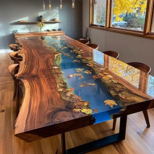Puede incluir: Una gran mesa de comedor hecha a medida con un diseño único. La mesa presenta una tapa de madera de borde vivo con un río de resina azul e incrustaciones de hojas de otoño. La mesa está soportada por una base de metal negro y rodeada de sillas de madera.
