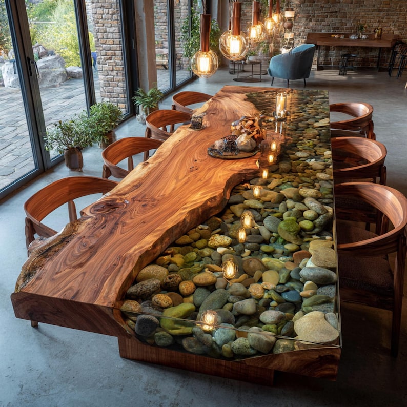 Pu&ograve; includere: Un grande tavolo da pranzo in legno realizzato su misura con un bordo vivo. Il tavolo presenta un intarsio in resina trasparente riempito di sassi di fiume, creando un'estetica naturale unica. Intorno al tavolo ci sono sedie di legno. Il tavolo &egrave; lungo circa 305 cm.