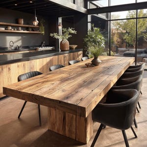 May include: A large, rectangular wooden dining table with a rustic, weathered appearance. The table is supported by a thick, solid wooden base and surrounded by several black leather chairs. The table is approximately 305 cm long.