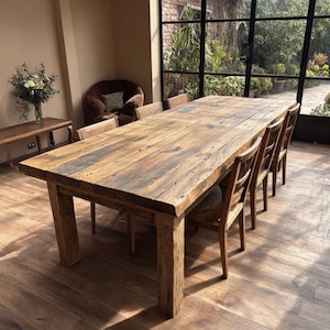 Puede incluir: Una gran mesa de comedor rectangular de madera con un aspecto rústico y envejecido. La mesa está rodeada de varias sillas de madera. La superficie de la mesa tiene una veta de madera natural y está sostenida por gruesas patas cuadradas.