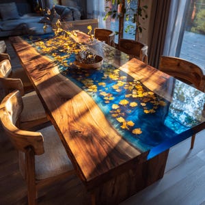 May include: A handcrafted wooden dining table with a blue epoxy river and embedded yellow leaf accents. The table is supported by a solid wooden base and surrounded by wooden chairs. The table measures approximately 100 inches long.
