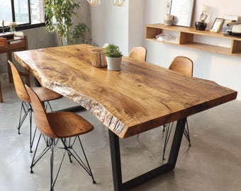 Puede incluir: Una mesa de comedor rectangular de madera grande con borde natural y base de metal negro. Cuatro sillas de madera con patas de alambre negro rodean la mesa. Una pequeña planta en maceta y objetos decorativos están sobre la mesa.