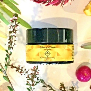 May include: A black jar with a gold label that reads "House of Venus Pure Organic Super-Collagen Activating Eye Gel". The jar is surrounded by white flowers and red berries.