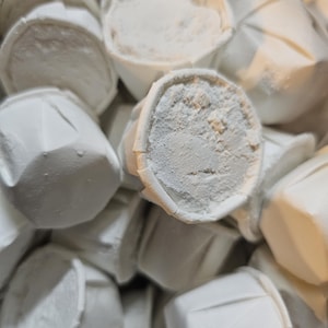 May include: Close-up of a collection of white, paper-like cups filled with a white powder. The cups have a folded design and are stacked together. The powder appears to be fine and granular.