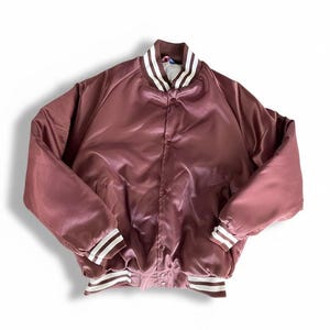 May include: A maroon satin bomber jacket with a white and maroon striped collar, cuffs, and hem. The jacket has a button-up front and a classic varsity style. The jacket is a medium size.