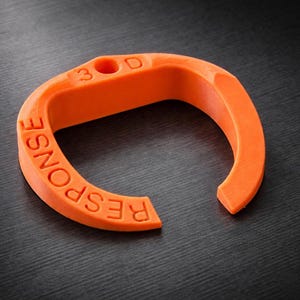 May include: A vibrant orange, curved object with the word "RESPONSE" embossed on its surface. It features a small hole and the letters "3 D". The item is set against a dark, textured background.
