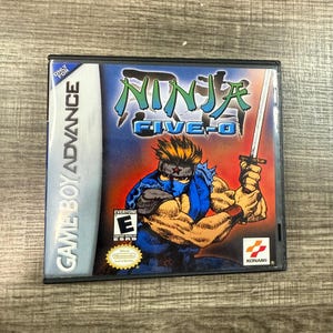 May include: A Game Boy Advance game cartridge for Ninja Five-O. The cover art features a muscular ninja in a blue outfit holding a sword, with the game title in blue and green. The game case is black.