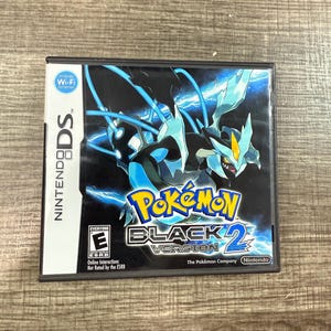 May include: A Nintendo DS game cartridge for Pokémon Black Version 2. The game case features a black background with a blue and white illustration of a Pokémon creature. The game title is in yellow and white.
