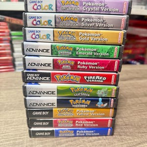 May include: A stack of Game Boy and Game Boy Advance video game cartridges. Titles include Pokémon Crystal Version, Silver Version, Gold Version, Emerald Version, Ruby Version, FireRed Version, LeafGreen, Sapphire, Yellow Version, Red Version, and Blue Version.