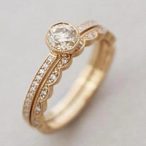 Peut inclure: Un ensemble de bagues de fiançailles en or. La bague principale présente un diamant rond dans un sertissage à festons. L'alliance assortie est ornée de petits diamants étincelants. L'ensemble est présenté sur un fond neutre.