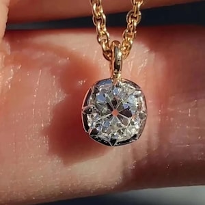 Puede incluir: Un collar de cadena dorada con un colgante redondo de diamante transparente. El diamante está engastado en un bisel de color plateado con un patrón de estrella. La cadena es un diseño delicado y enlazado.