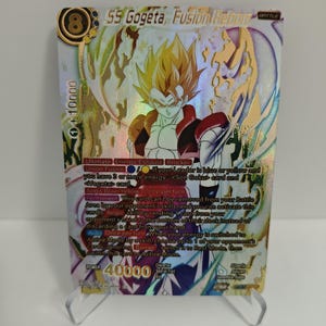 Puede incluir: Una tarjeta coleccionable holográfica con SS Gogeta de Fusion Reborn. La tarjeta tiene un borde dorado y presenta un personaje con cabello amarillo puntiagudo y un atuendo rojo y blanco. El poder de la tarjeta es 40.000.