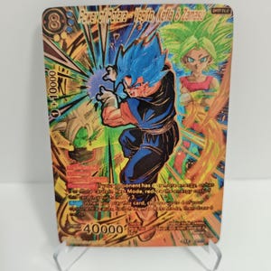 Könnte beinhalten: Eine holografische Sammelkarte mit Charakteren aus der Dragon Ball-Serie. Die Karte hat ein Gold- und Blau-Farbschema mit dem Text "Power of Potara - Vegito, Kefla & Zamasu". Die Karte steht auf einem transparenten Ständer.
