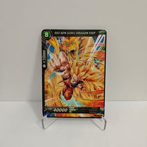 May include: A trading card depicting a character with spiky yellow hair and orange attire. The card reads "SS3 SON GOKU DRAGON FIST" and has the number "8". The card is presented on a clear plastic stand.