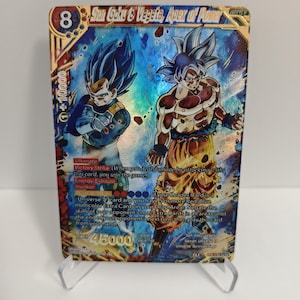 Może przedstawiać: Holograficzna karta kolekcjonerska z Son Goku i Vegetą, Apex of Power. Karta ma złote obramowanie i zawiera tekst oraz statystyki mocy. Postacie są w dynamicznych pozach, z żywymi kolorami niebieskim i pomarańczowym.