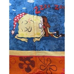 May include: A blue and orange patterned fabric featuring a sleeping cartoon character wearing a red and white polka dot nightcap. The character is yellow with black eyes and a brown body. The word "Z" is repeated three times at the top.