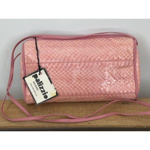 May include: A cylindrical pink handbag with a textured reptile skin pattern and a thin shoulder strap. A white rectangular tag attached by a black string features the text Palizzio Accessc Genuine Reptile in black lettering on the front.