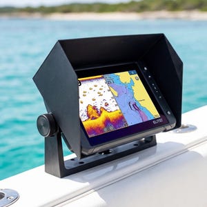 May include: A white ceramic mug with a black handle and the text "But First, Coffee" in a bold, black font. The mug is set against a blurred background. The mug appears to be approximately 10 cm tall.