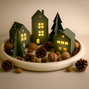 May include: A decorative holiday display featuring miniature green houses and trees with illuminated windows, pinecones, and walnuts arranged on a white, round tray. The scene evokes a cozy, festive atmosphere.
