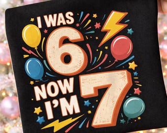 以下が含まれることがあります： I WAS 6 NOW I'M 7というテキストがプリントされた黒い布製品。大きなベージュの数字の6と7が中央に配置され、その周囲には黄色、青、赤のカラフルな風船と、黄色の稲妻のイラストが描かれています。